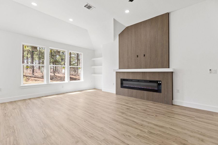 Unfurnished living room featuring a glass covered fireplace, light wood-type flooring, vaulted ceiling, and recessed lighting