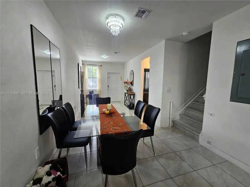 Neutral-toned floor tiling, wall-mounted mirrored paneling, recessed lighting, tiered crystal-style chandelier, and staircase with wood-finish treads