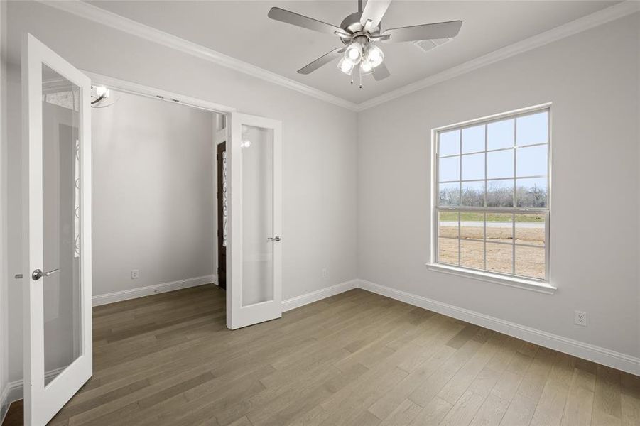 Spare room with french doors, wood finished floors, baseboards, ornamental molding, and a ceiling fan Spare room with french doors, wood finished floors, baseboards, ornamental molding, and a ceiling fan