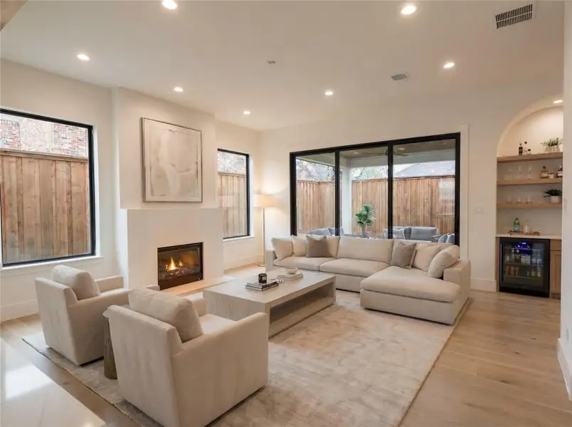 Living Room- Gas fireplace, engineered wide-plank floors, sliding glass doors to covered patio, built-in bar with beverage fridge, and a signature arched alcove — warm, refined, and effortlessly livable. (Rendering)