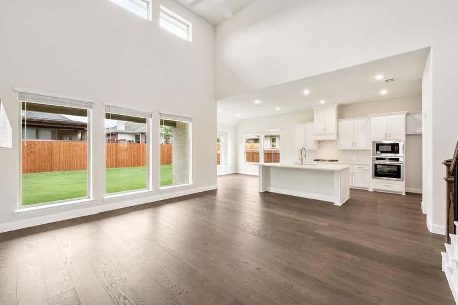 Open living area with high ceilings and hardwood floors flowing into white kitchen with island and stainless appliances