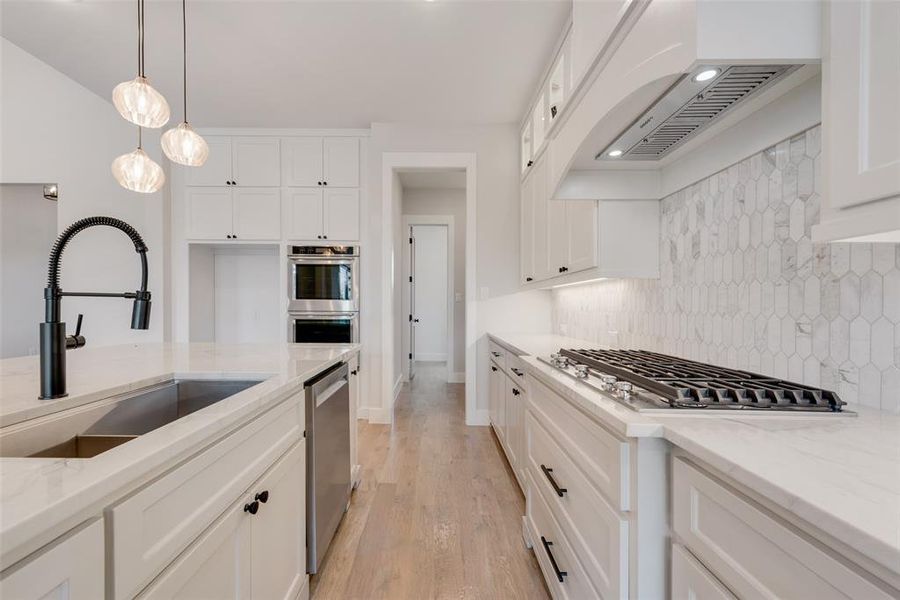 Kitchen with light stone countertops, stainless steel appliances, light wood-type flooring, backsplash, and white cabinets