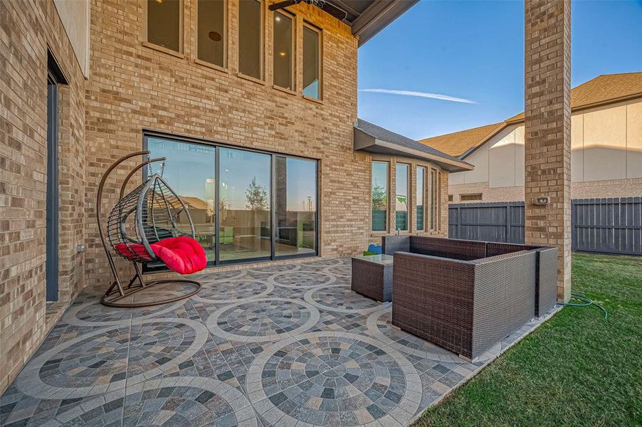 The covered extended patio, adorned with decorative brick pavers, overlooks a sprawling backyard perfect for entertaining.