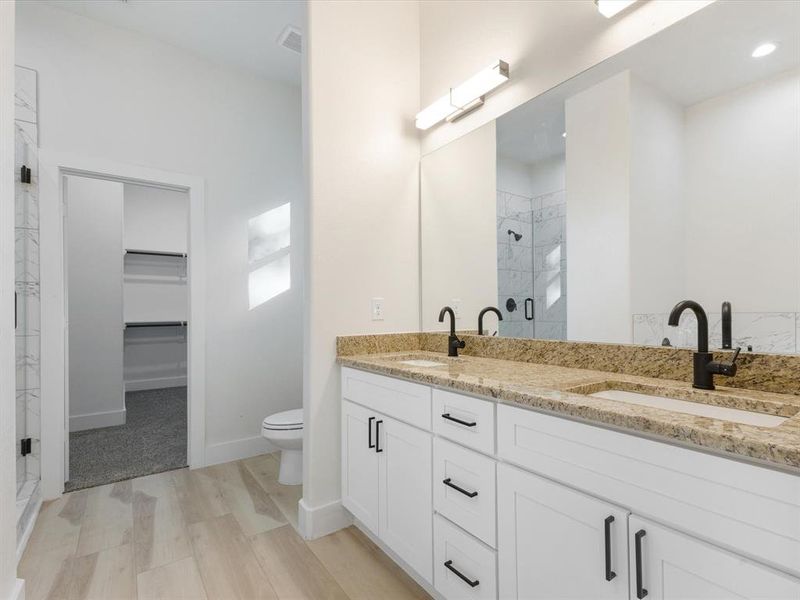 Full bathroom featuring a walk in closet, a stall shower, double vanity, and light wood-style flooring