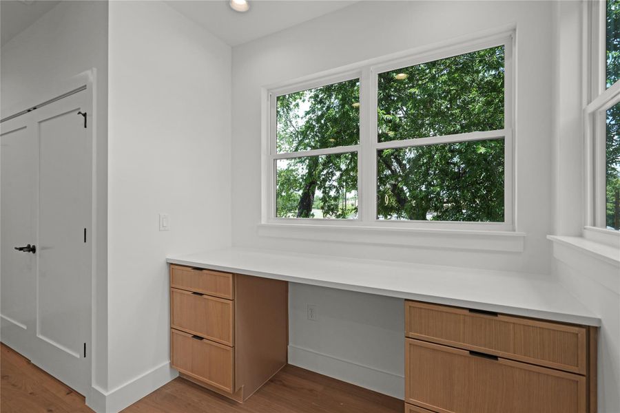 A dedicated home office space with built-in cabinetry and expansive windows framing verdant views.