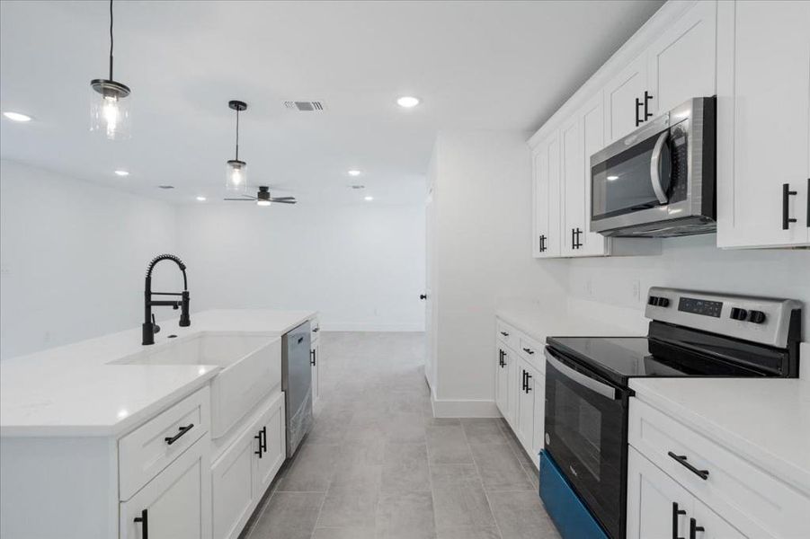 Kitchen with pendant lighting, an island with sink, stainless steel appliances, ceiling fan, and white cabinets