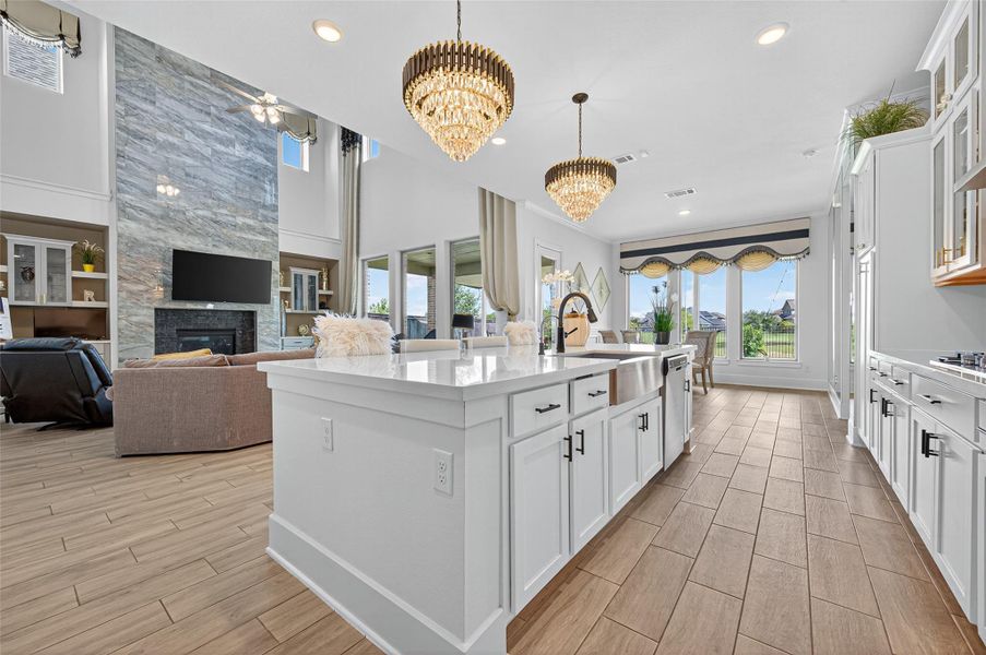 This spacious, open-concept living area features a modern kitchen with a large island, elegant chandeliers, and ample natural light. The adjacent living room boasts a sleek fireplace and high ceilings, creating a luxurious and inviting atmosphere. This spacious, open-concept living area features a modern kitchen with a large island, elegant chandeliers, and ample natural light. The adjacent living room boasts a sleek fireplace and high ceilings, creating a luxurious and inviting atmosphere.