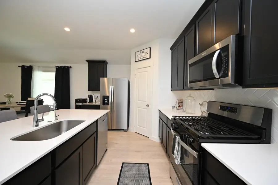 Modern kitchen with sleek dark cabinetry, stainless steel appliances, and white countertops. Features a large island with a sink and an open layout leading to a dining area. Modern kitchen with sleek dark cabinetry, stainless steel appliances, and white countertops. Features a large island with a sink and an open layout leading to a dining area.