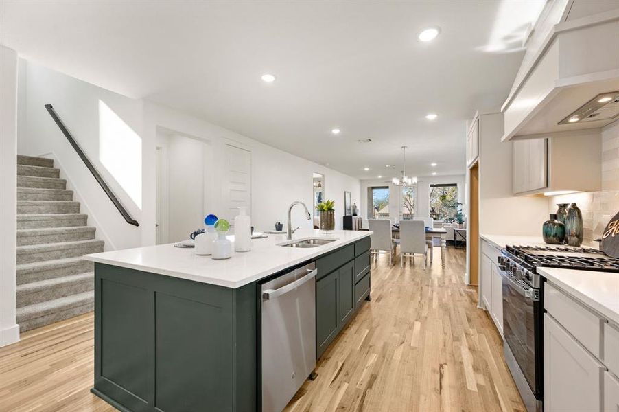 Kitchen with two tone color scheme, range with gas stovetop, dishwasher, a center island with sink, and light wood finished floors