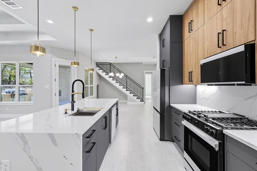 Kitchen with black gas range oven, decorative light fixtures, recessed lighting, light stone counters, and modern cabinets