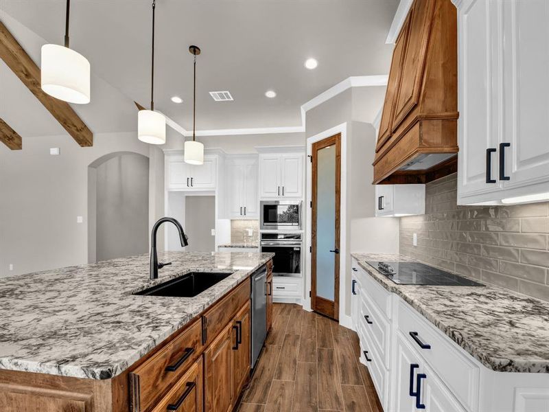 Kitchen with an island with sink, brown cabinets, white cabinetry, decorative light fixtures, and recessed lighting