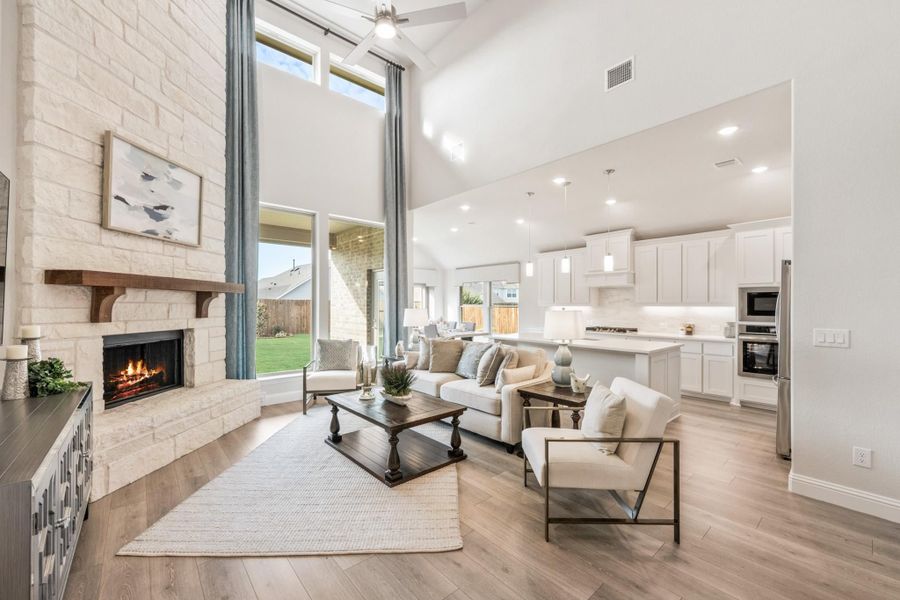 Open-concept living room with two-story stone fireplace, vaulted ceiling, and view into white kitchen Open-concept living room with two-story stone fireplace, vaulted ceiling, and view into white kitchen