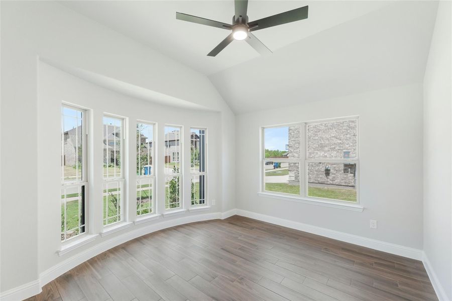 Empty room with vaulted ceiling, ceiling fan, hardwood floors, and large windows with neighborhood views Empty room with vaulted ceiling, ceiling fan, hardwood floors, and large windows with neighborhood views
