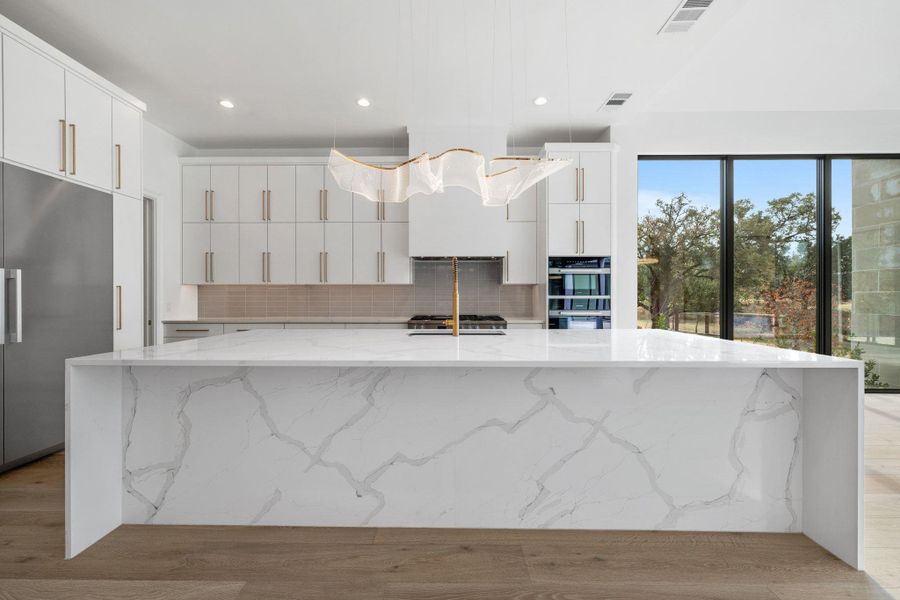 Kitchen with a large island with sink, stainless steel appliances, light stone countertops, and light wood finished floors