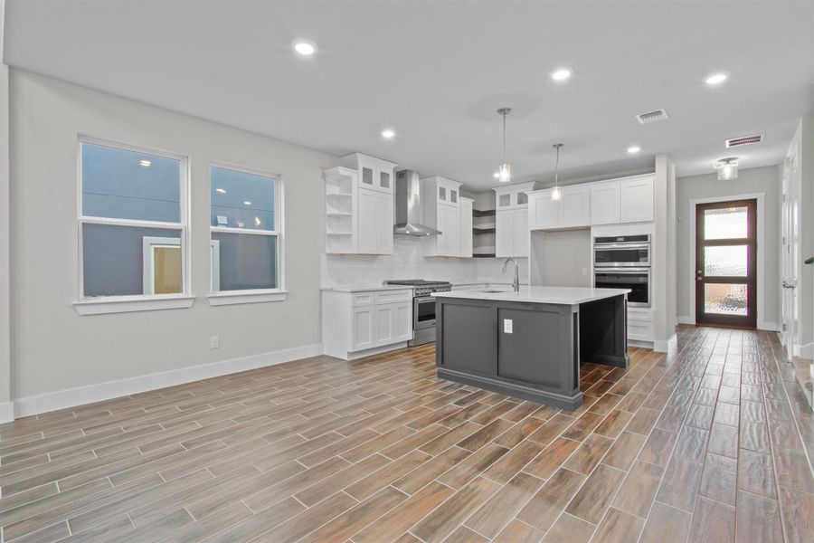 Kitchen with hanging light fixtures, appliances with stainless steel finishes, an island with sink, white cabinets, and wall chimney exhaust hood