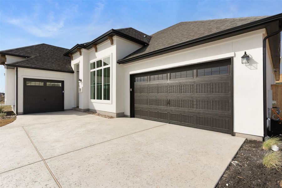 View of front facade with roof with shingles, an attached garage, driveway, and stucco siding