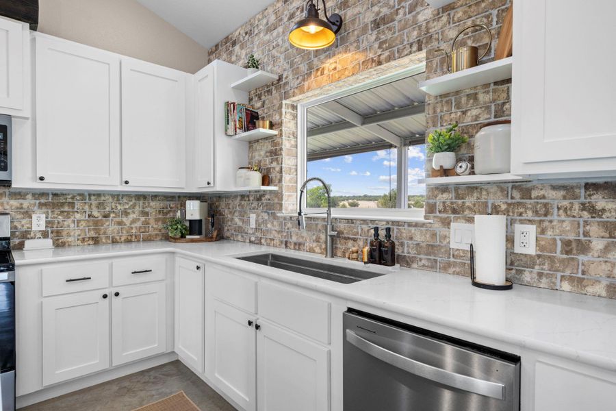 Kitchen featuring open shelves, white cabinetry, stainless steel dishwasher, and light stone countertops