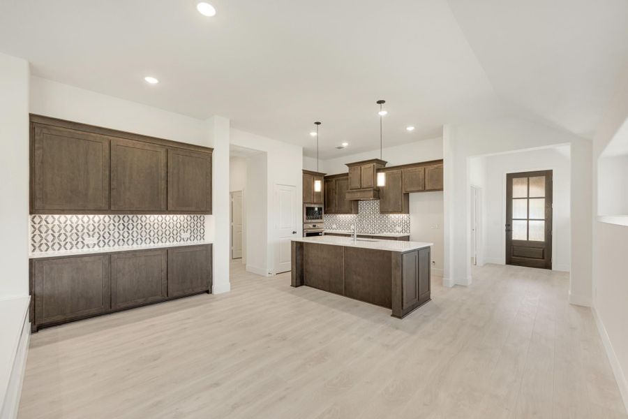 Open kitchen with dark brown cabinets, center island, patterned tile backsplash, and light wood floors