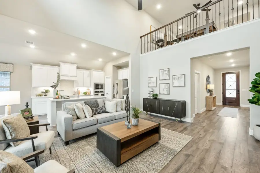 Open-concept living room with vaulted ceiling, hardwood floors, and kitchen visible in background