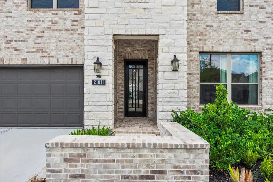 Receive a warm welcome every time with this inviting front entry, where timeless brick and stone accents, stylish coach lighting, and a charming covered porch are framed by lush, well-manicured landscaping.