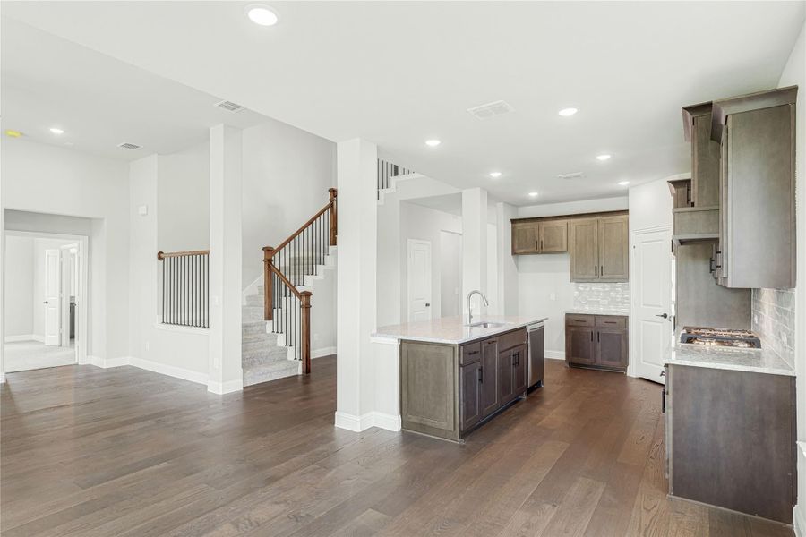 Open-concept kitchen with dark wood cabinets, center island, and hardwood floors open to living area and staircase Open-concept kitchen with dark wood cabinets, center island, and hardwood floors open to living area and staircase