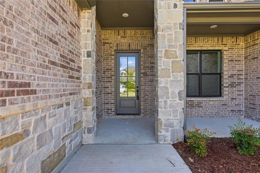 Covered entry featuring a paneled front door with glass inserts, flanked by brick and stone veneer