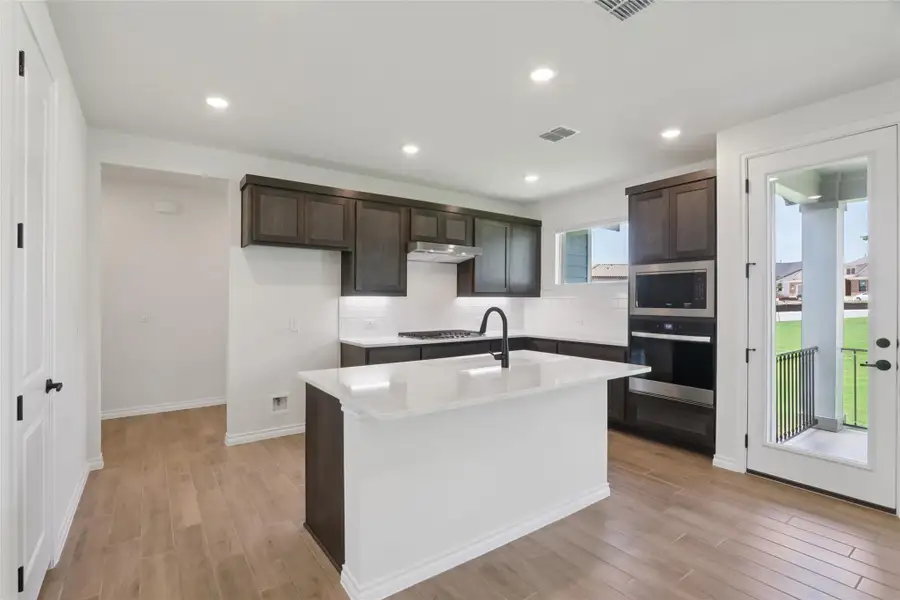 Kitchen with light wood finished floors, stainless steel appliances, dark brown cabinetry, tasteful backsplash, and light countertops