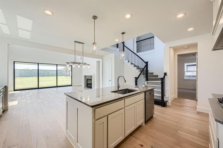 Kitchen with a sink, stainless steel dishwasher, light wood-style flooring, a glass covered fireplace, and open floor plan Kitchen with a sink, stainless steel dishwasher, light wood-style flooring, a glass covered fireplace, and open floor plan