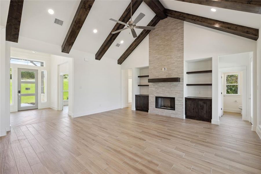 Unfurnished living room with a stone fireplace, high vaulted ceiling, light hardwood / wood-style floors, and beam ceiling