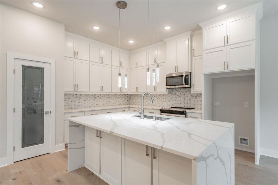 Kitchen featuring light stone countertops, a center island with sink, light wood-type flooring, recessed lighting, and appliances with stainless steel finishes