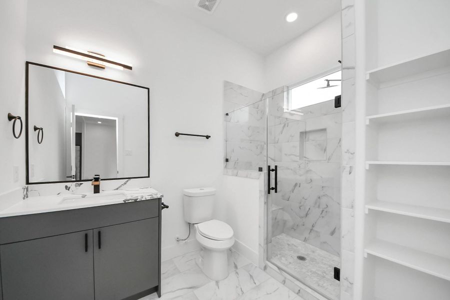 This bathroom features a modern design with a sleek vanity, large mirror, and elegant lighting. It has a spacious glass-enclosed shower with marble-style tiles and built-in shelving for storage. This bathroom features a modern design with a sleek vanity, large mirror, and elegant lighting. It has a spacious glass-enclosed shower with marble-style tiles and built-in shelving for storage.