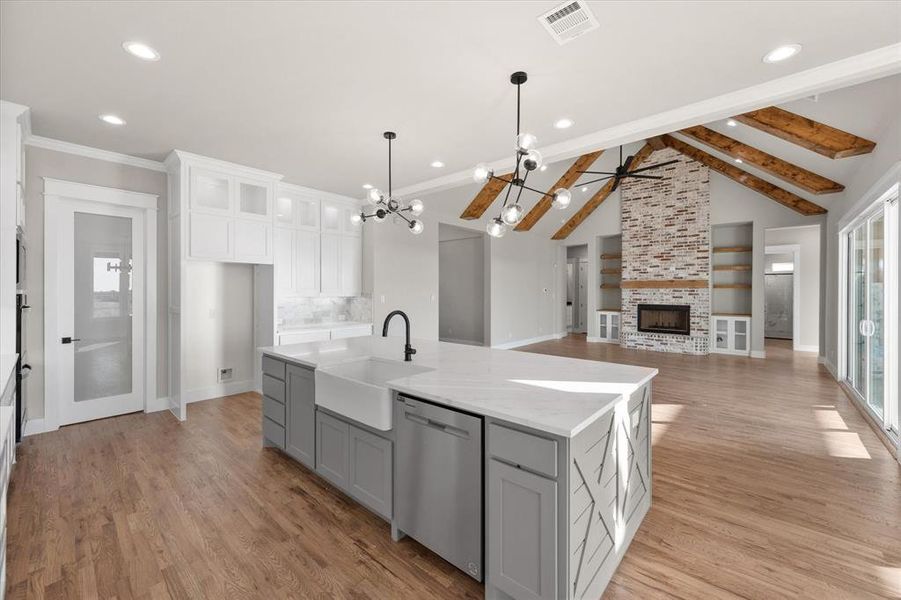 Kitchen featuring sink, dishwasher, an island with sink, a fireplace, and white cabinetry