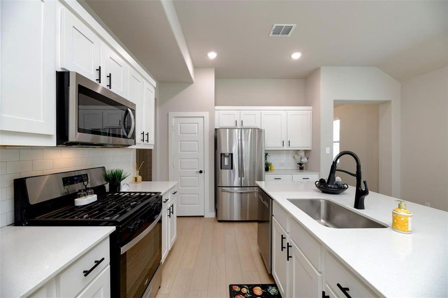 Kitchen with stainless steel appliances, white cabinetry, backsplash, light stone countertops, and recessed lighting Kitchen with stainless steel appliances, white cabinetry, backsplash, light stone countertops, and recessed lighting