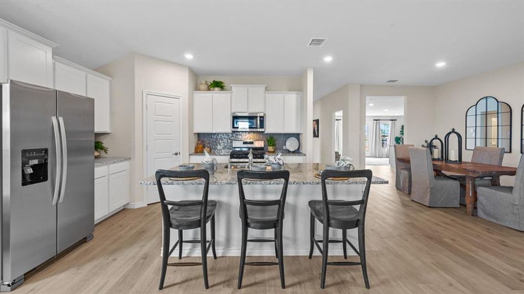 Kitchen featuring stainless steel appliances, white cabinetry, a kitchen island with sink, a breakfast bar, and light wood-style flooring Kitchen featuring stainless steel appliances, white cabinetry, a kitchen island with sink, a breakfast bar, and light wood-style flooring