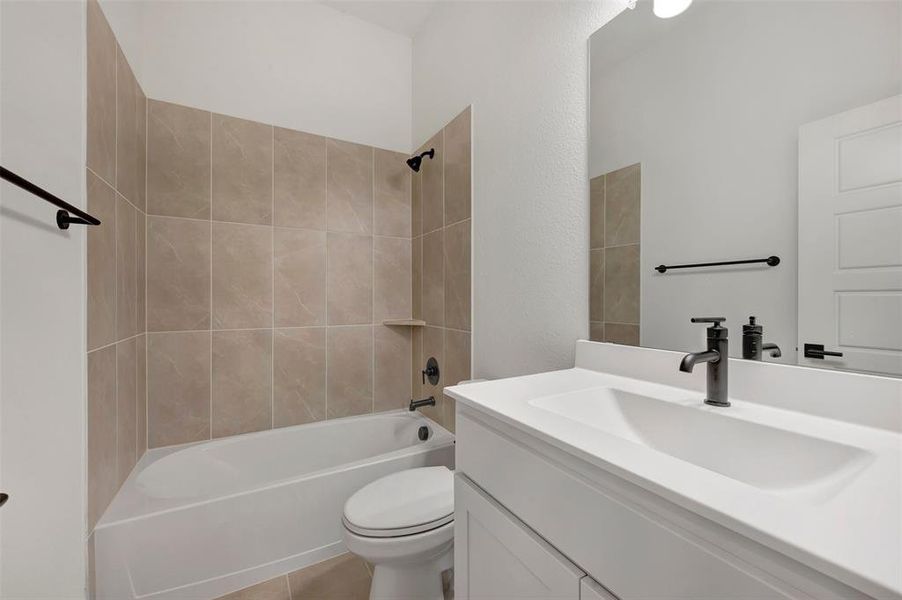 Bathroom featuring a white vanity with an integrated sink, matte black fixtures, a rectangular mirror, a bathtub with a tiled surround, and a built-in shower niche