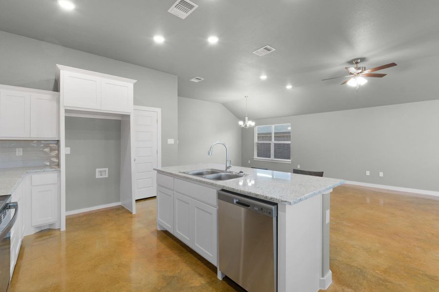 A well-lit kitchen with granite countertops and stainless steel appliances, opening to a spacious living area.