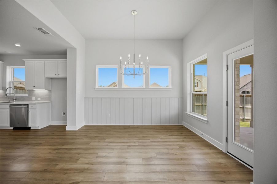A sleek chandelier illuminates this spacious dining area with wood flooring and wainscoting details.