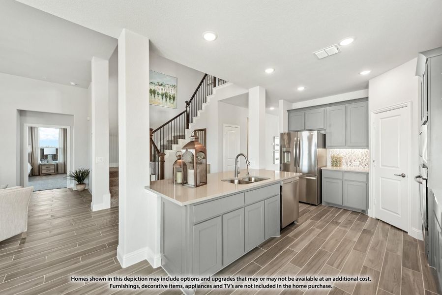 Kitchen with gray cabinets, center island with sink, stainless steel appliances, and wood-look tile floors open to staircase. Kitchen with gray cabinets, center island with sink, stainless steel appliances, and wood-look tile floors open to staircase.