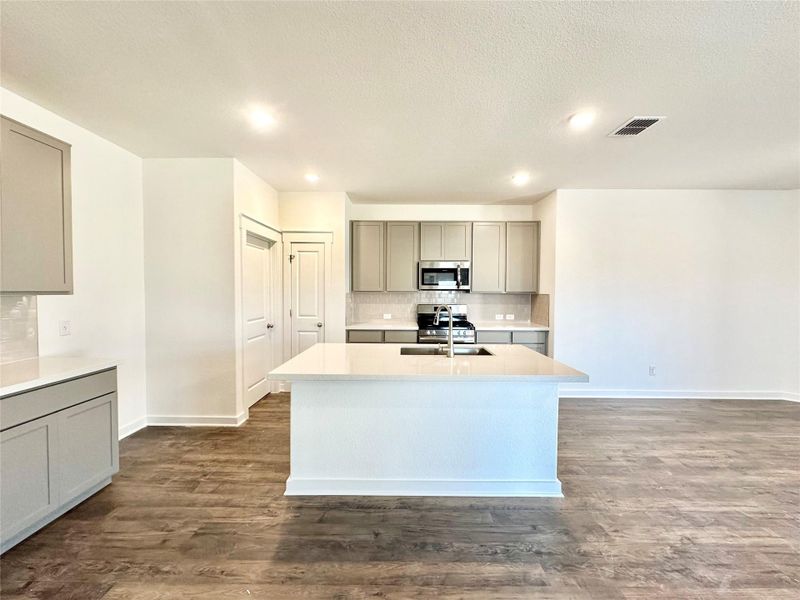 Kitchen featuring gray cabinetry, an island with sink, tasteful backsplash, dark wood finished floors, and recessed lighting