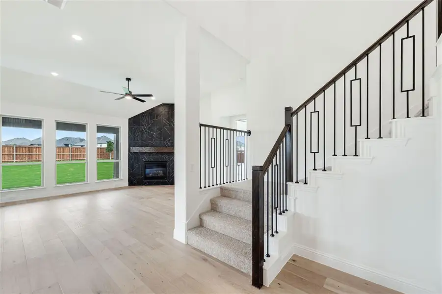 Carpeted staircase with dark wood and iron railing beside open living room with marble fireplace and hardwood floors
