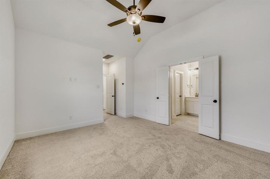 Unfurnished bedroom featuring light colored carpet, vaulted ceiling, ceiling fan, and ensuite bath Unfurnished bedroom featuring light colored carpet, vaulted ceiling, ceiling fan, and ensuite bath