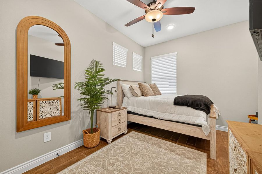 Spacious secondary bedroom with wood-look flooring, modern ceiling fan, and stylish design touches. Spacious secondary bedroom with wood-look flooring, modern ceiling fan, and stylish design touches.