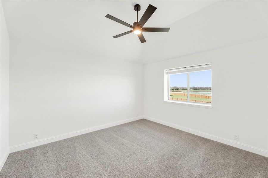 Empty bedroom with vaulted ceiling, ceiling fan, gray carpet, and window with backyard view Empty bedroom with vaulted ceiling, ceiling fan, gray carpet, and window with backyard view