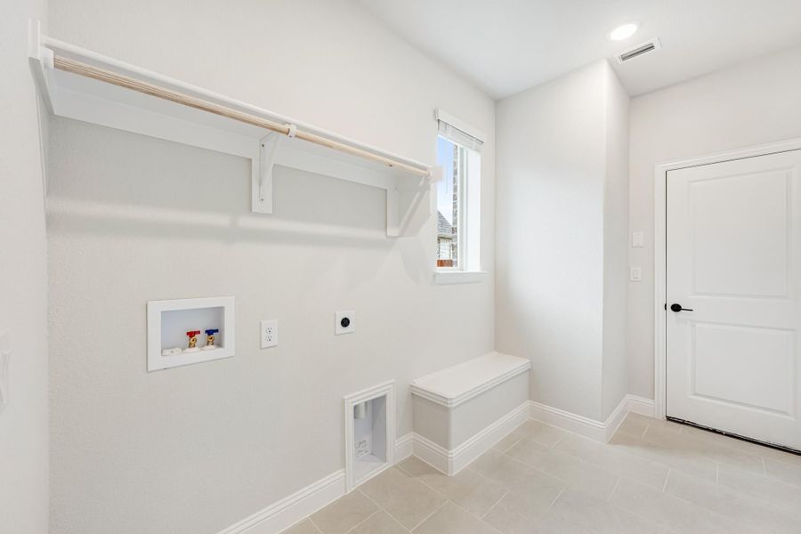 Laundry room with wall-mounted drying rod, shelf, washer hookups, and a small built-in bench on tile floor