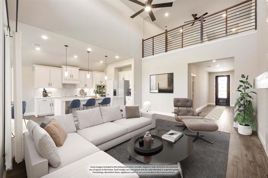 Open-concept living room with two-story ceiling, ceiling fan, and view of white kitchen and upper loft railing Open-concept living room with two-story ceiling, ceiling fan, and view of white kitchen and upper loft railing