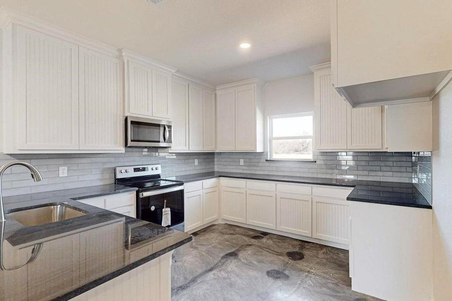 Kitchen featuring dark stone countertops, a sink, stainless steel appliances, white cabinetry, and backsplash