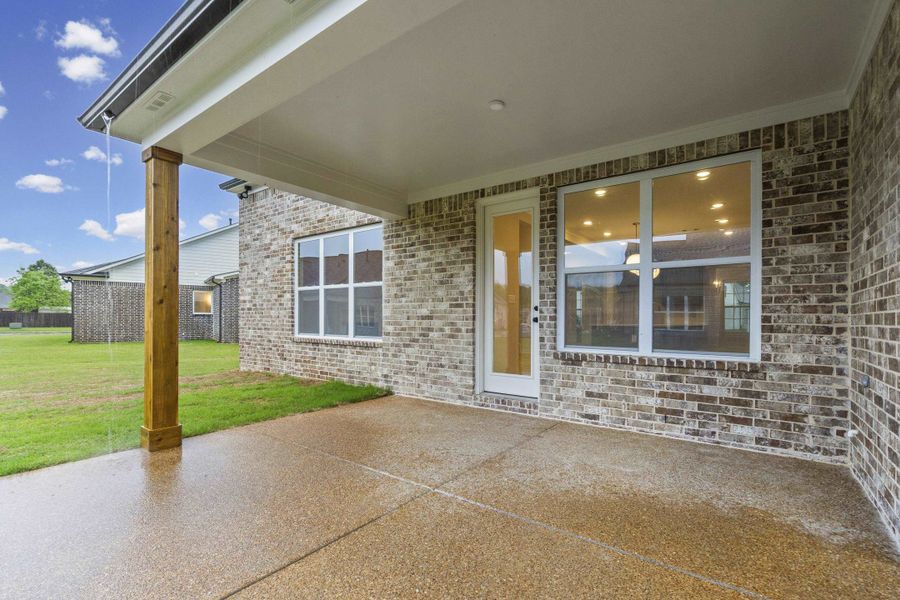 Covered patio featuring a stained wood post, exposed aggregate concrete flooring, and a brick exterior Covered patio featuring a stained wood post, exposed aggregate concrete flooring, and a brick exterior
