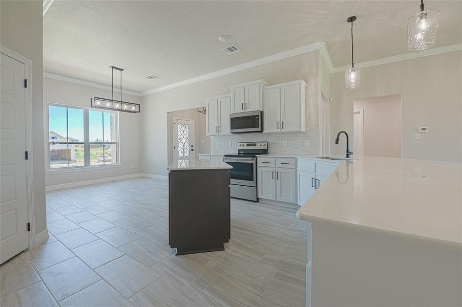 Kitchen featuring hanging light fixtures, white cabinets, stainless steel appliances, crown molding, and tasteful backsplash