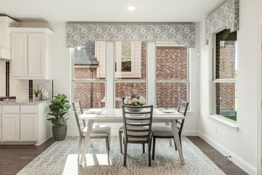 Breakfast nook with white dining table, four chairs, large windows, and patterned valances near white kitchen cabinets