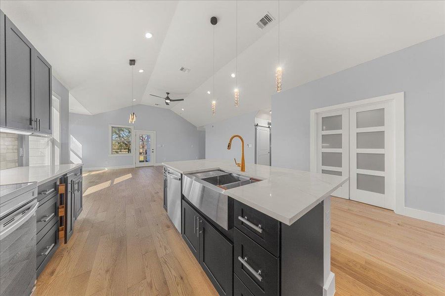 Kitchen with dark cabinets, pendant lighting, lofted ceiling, light wood-style floors, and light stone counters Kitchen with dark cabinets, pendant lighting, lofted ceiling, light wood-style floors, and light stone counters